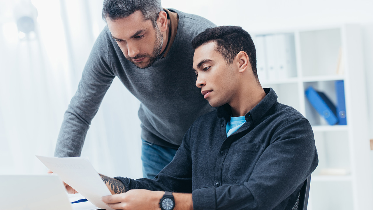 Mentor looking at young protege working with papers in office