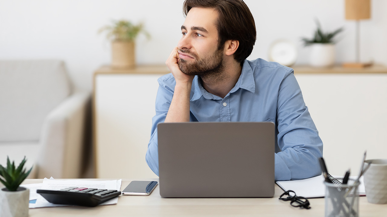 Bored businessman sitting at laptop, looking aside and procrastinating