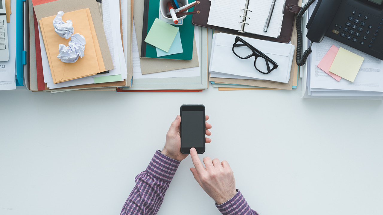 Businessman working at office desk and using a business app on a touch screen smartphone