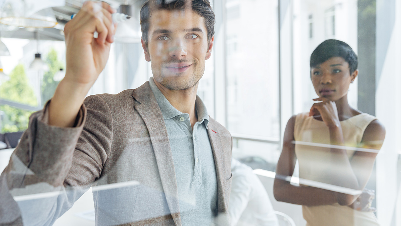 Businessman working with businesswoman and writing on transparent board