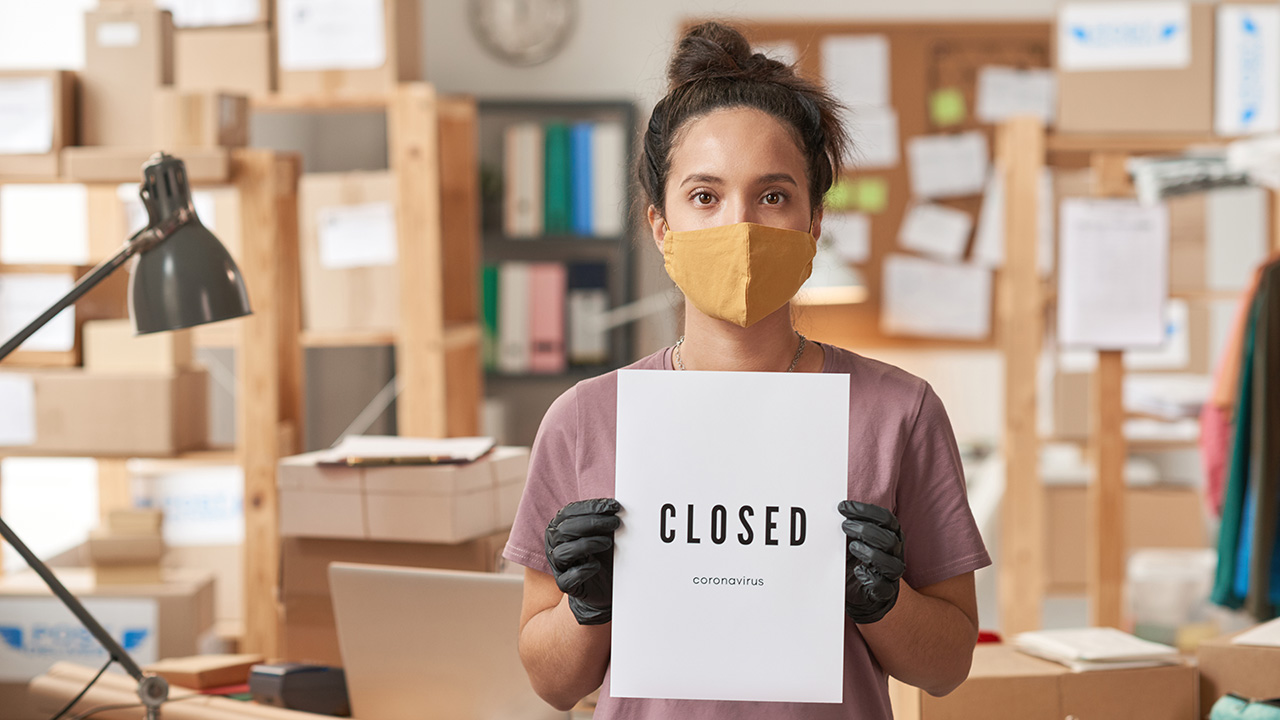 Young woman in protective mask holding a CLOSED sign