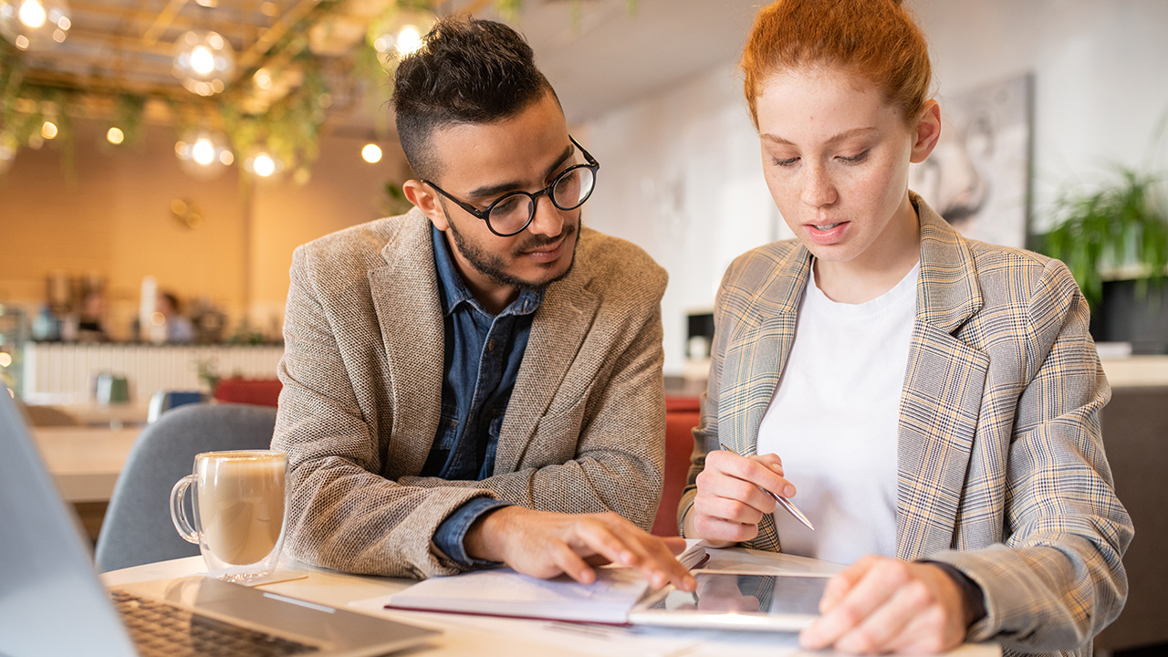 Young businessman scrolling in touchpad while showing his colleague some new creative ideas