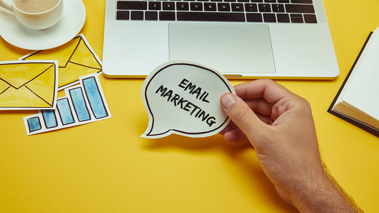 Man holding speech bubble with 'email marketing' lettering near laptop