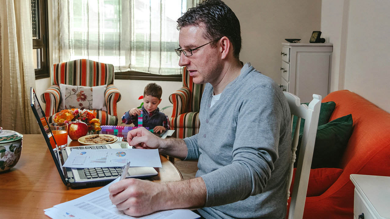 Father working on the laptop in the living room while his son plays