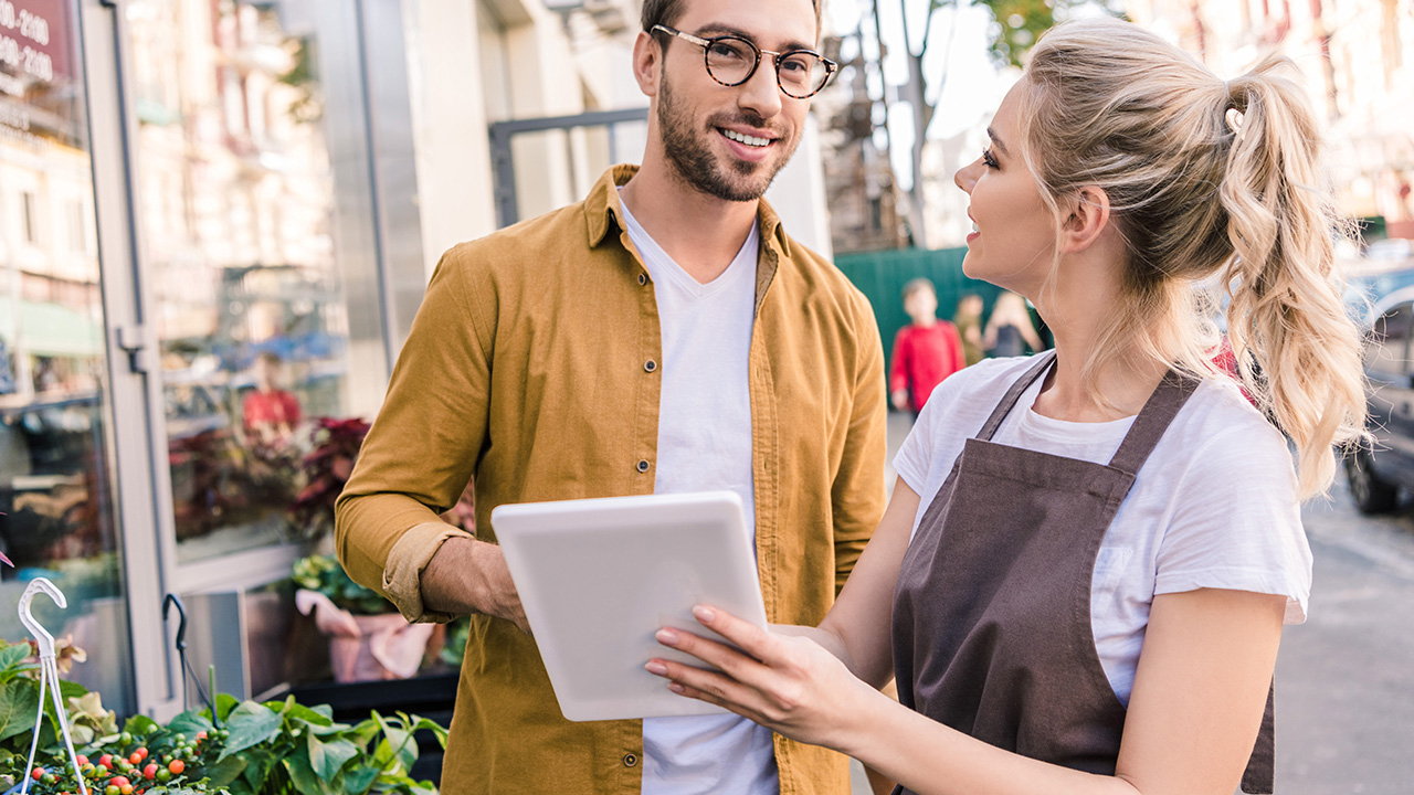 Florist and smiling customer using tablet at flower shop