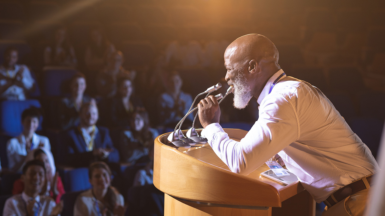Old businessman speaking to audience in an auditorium