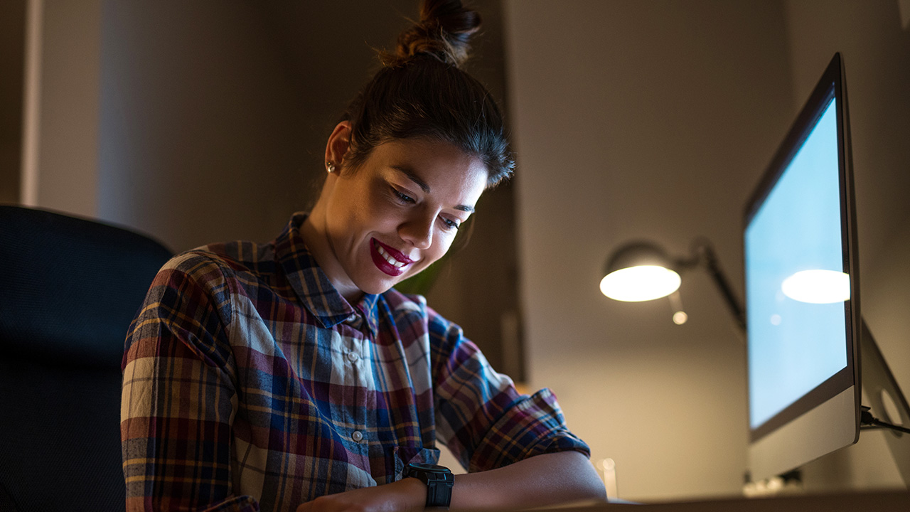 Smiling satisfied young businesswoman working late at night