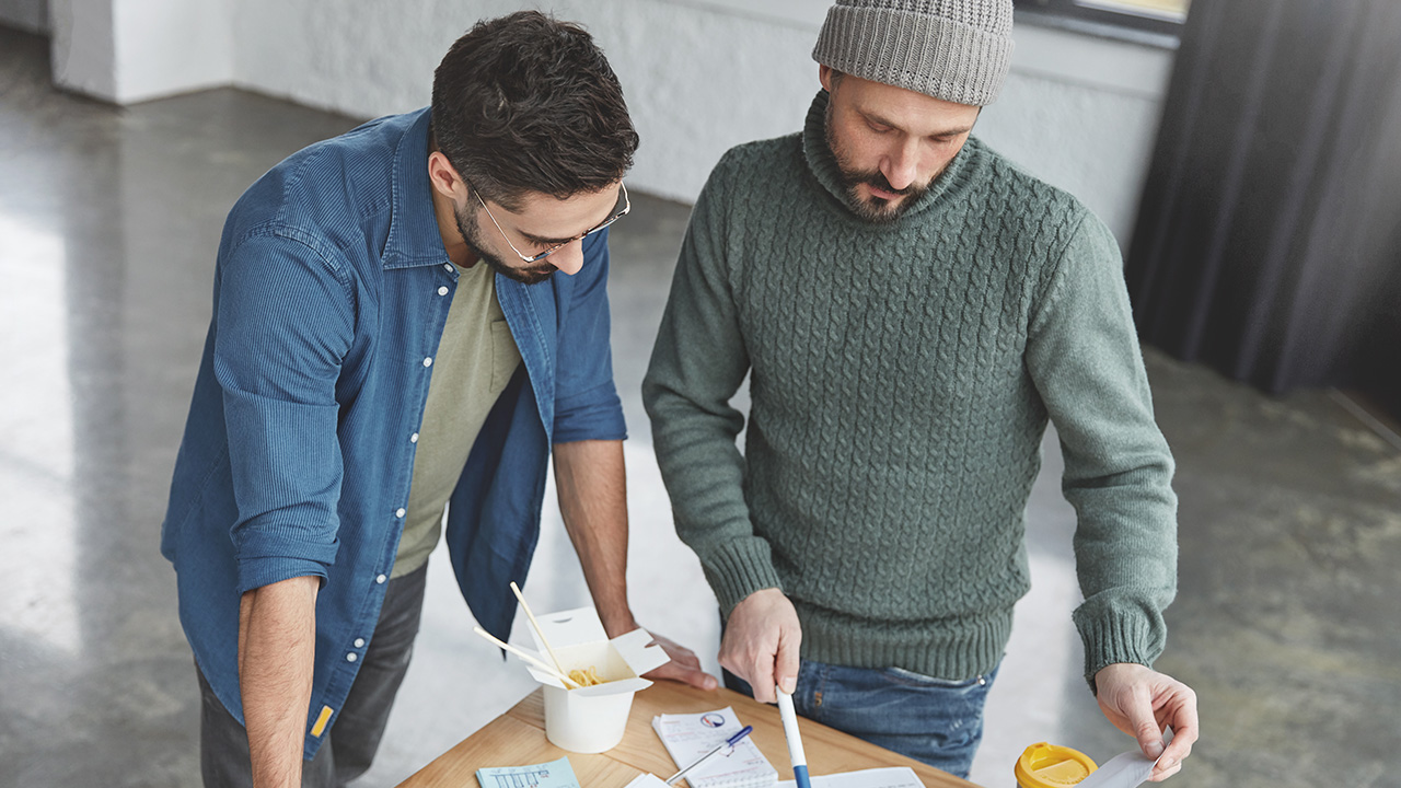 Two stylish bussinesmen stand near working desk