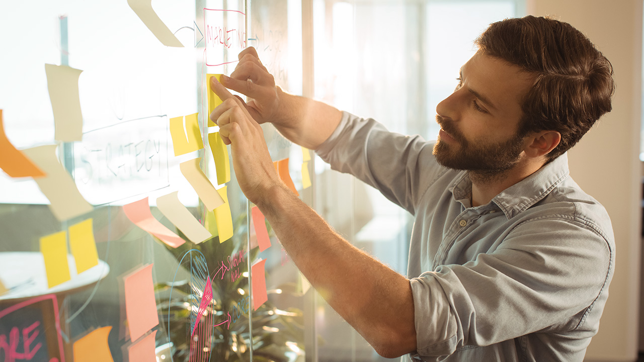 Young businessman sticking adhesive notes on glass at office