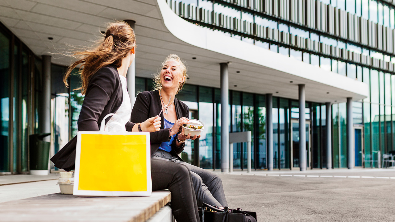 Two Women Eating Salad by Office Building and Laughing