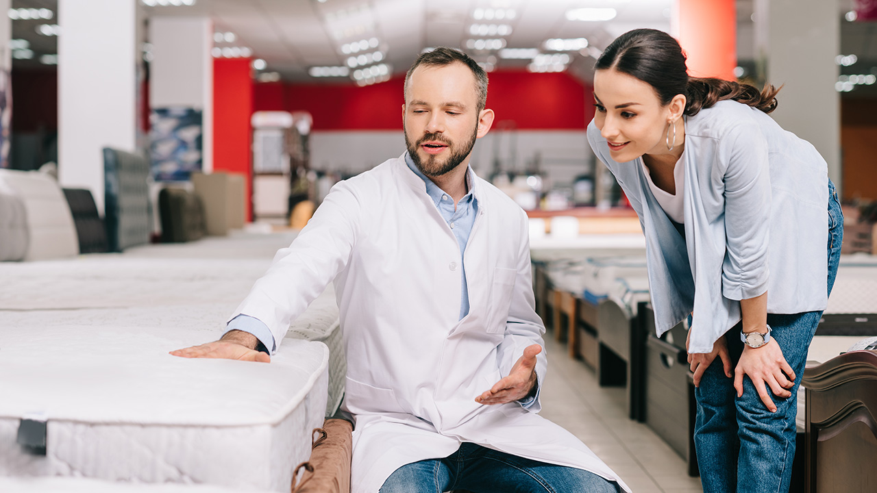 Mattress Salesman Showing Female Customer a Mattress in a Furniture Store